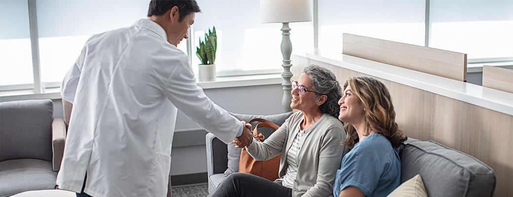 Image of hearing care professional greeting senior woman and her daughter in a waiting room